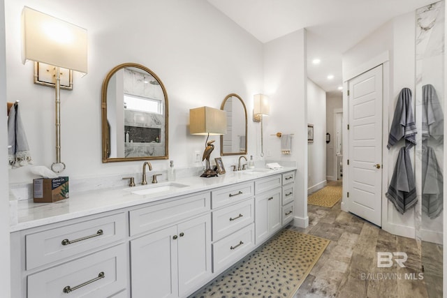 full bath with double vanity, wood finished floors, a sink, and baseboards