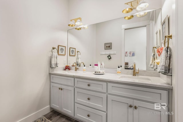 full bathroom with double vanity, wood finished floors, a sink, and baseboards