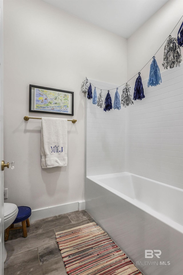 bathroom with a bathtub, toilet, baseboards, and wood finished floors