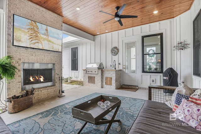 living room with an outdoor brick fireplace, recessed lighting, wooden ceiling, and a decorative wall