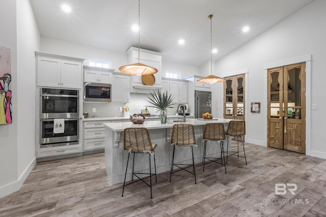 kitchen with stainless steel appliances, light wood-style floors, light countertops, a kitchen bar, and a center island with sink