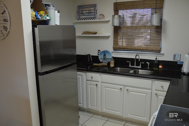 kitchen with light tile patterned floors, a sink, white cabinetry, freestanding refrigerator, and dark countertops