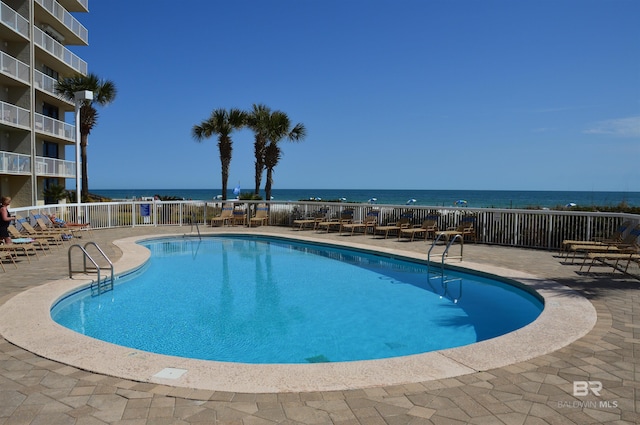 community pool featuring a water view, a patio area, and fence