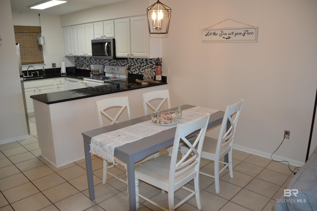 kitchen featuring light tile patterned floors, white cabinets, stainless steel microwave, a peninsula, and white range with electric cooktop