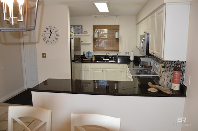 kitchen featuring stainless steel appliances, dark countertops, white cabinetry, a sink, and a peninsula