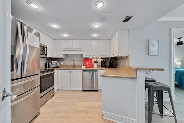 kitchen featuring a kitchen bar, kitchen peninsula, white cabinetry, and appliances with stainless steel finishes