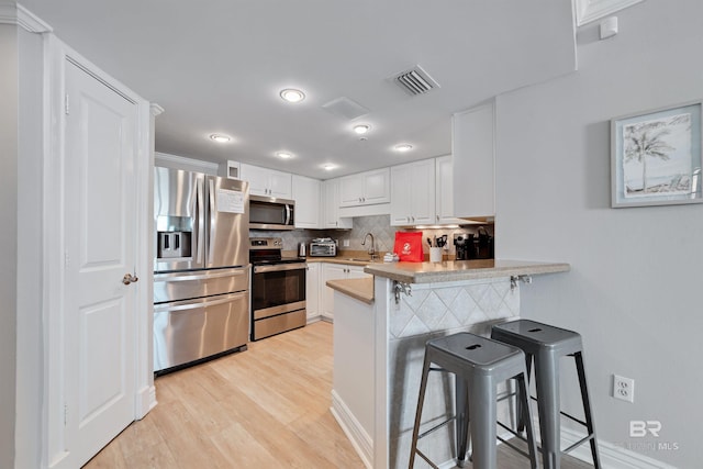 kitchen with white cabinetry, a kitchen breakfast bar, kitchen peninsula, appliances with stainless steel finishes, and light wood-type flooring