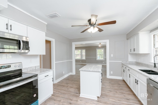 kitchen with appliances with stainless steel finishes, light stone counters, sink, white cabinets, and a center island