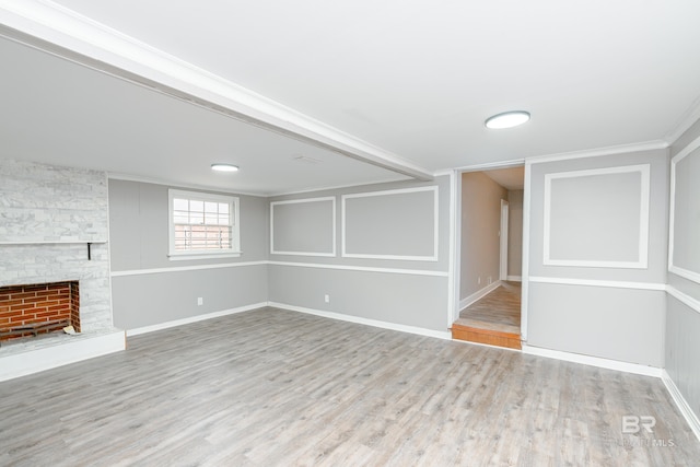 basement with light hardwood / wood-style floors, a stone fireplace, and crown molding