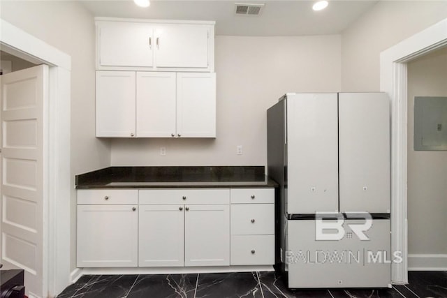 kitchen featuring white refrigerator, electric panel, and white cabinetry