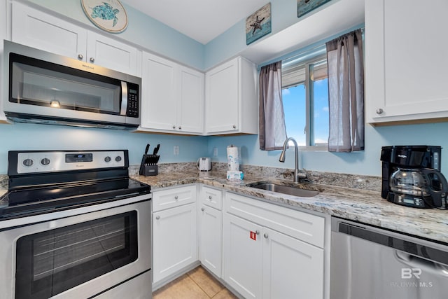 kitchen with sink, white cabinets, light tile patterned floors, appliances with stainless steel finishes, and light stone counters