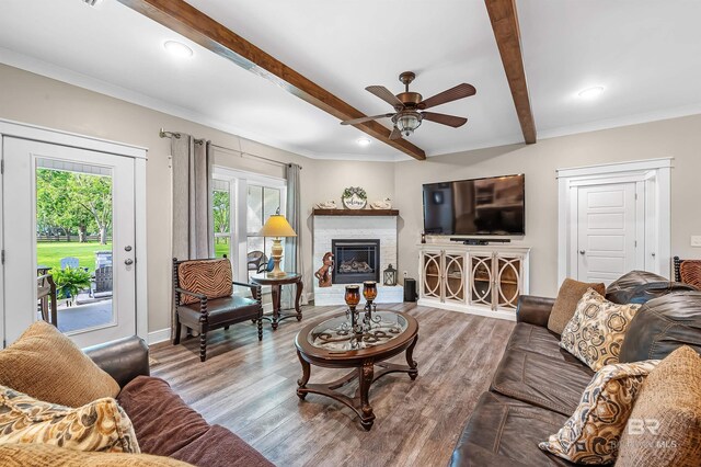 living room featuring hardwood / wood-style floors, ceiling fan, beam ceiling, and a brick fireplace