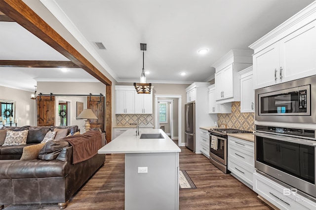 kitchen with white cabinetry, a barn door, a kitchen island with sink, and stainless steel appliances