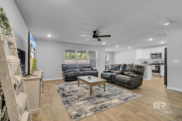 living room featuring ceiling fan, light wood-type flooring, and a textured ceiling