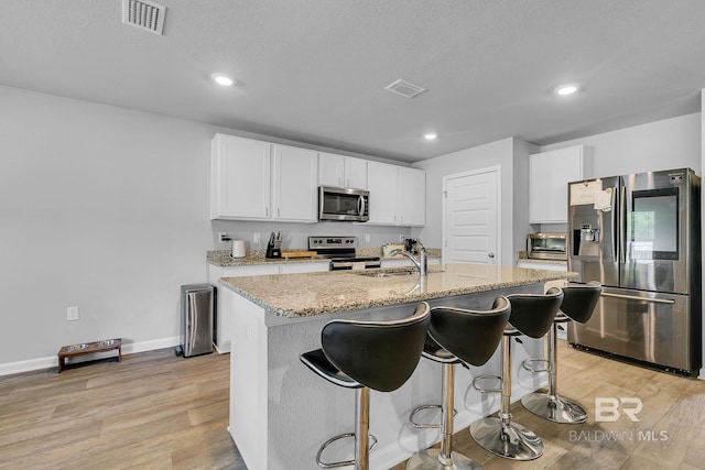 kitchen with white cabinetry, a center island with sink, light hardwood / wood-style floors, and stainless steel appliances