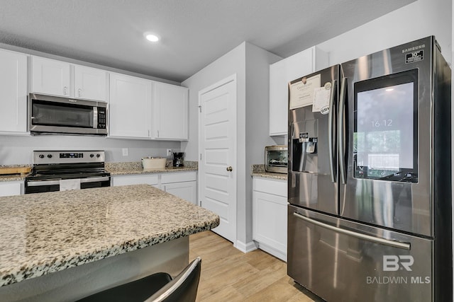 kitchen featuring white cabinets, light stone counters, light wood-type flooring, and stainless steel appliances