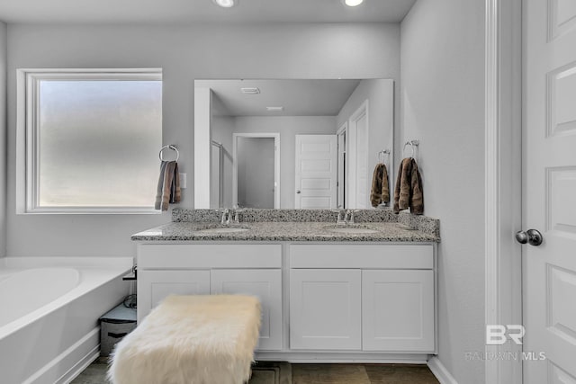 bathroom featuring a bath to relax in, double vanity, and a wealth of natural light