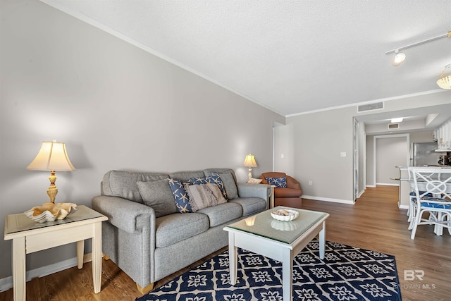 living room featuring a textured ceiling, baseboards, visible vents, wood finished floors, and ornamental molding