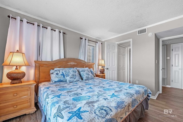bedroom with wood finished floors, visible vents, a textured ceiling, and crown molding
