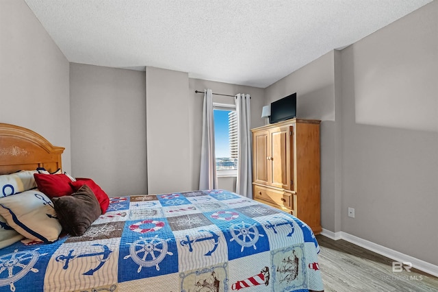 bedroom with wood finished floors, a textured ceiling, and baseboards