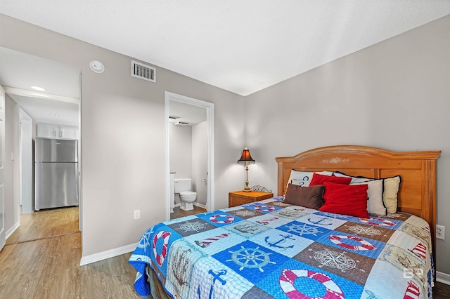 bedroom with wood finished floors, connected bathroom, baseboards, visible vents, and freestanding refrigerator