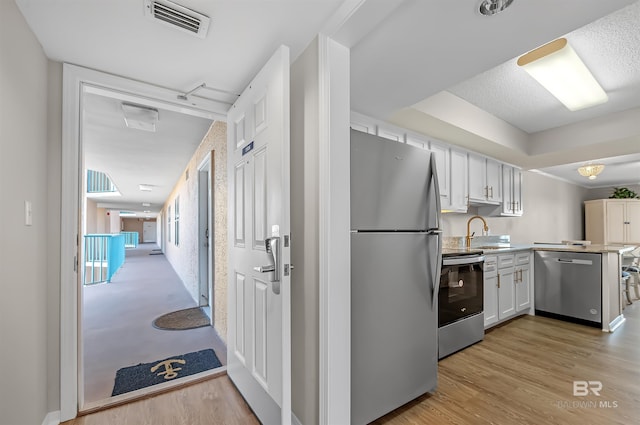 kitchen featuring a sink, light wood-style floors, stainless steel appliances, a peninsula, and visible vents
