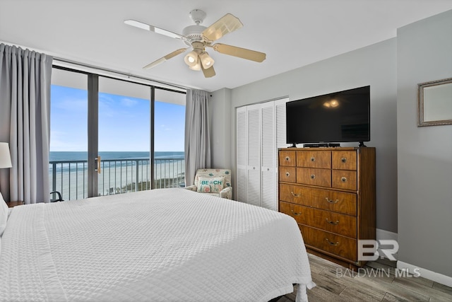 bedroom with a closet, access to exterior, hardwood / wood-style floors, a water view, and ceiling fan