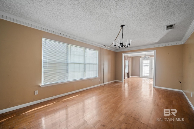 unfurnished room featuring a textured ceiling, wood-type flooring, crown molding, and a chandelier