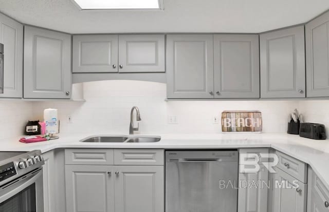 kitchen with light countertops, a sink, stainless steel appliances, gray cabinetry, and backsplash