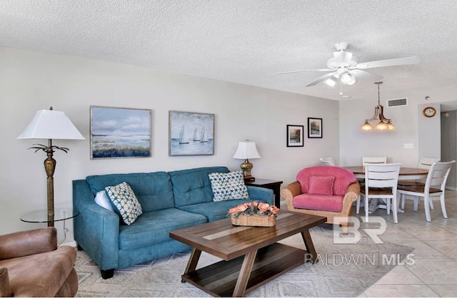 living area featuring visible vents, a ceiling fan, light tile patterned flooring, and a textured ceiling