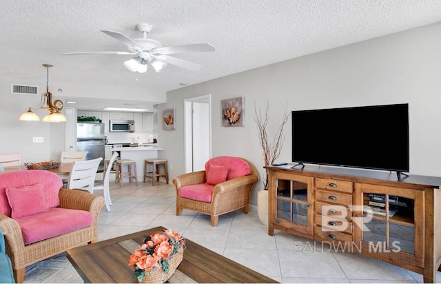 living room featuring visible vents, ceiling fan, light tile patterned floors, and a textured ceiling