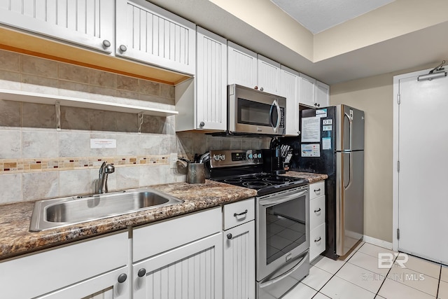 kitchen featuring light tile patterned floors, stainless steel appliances, a sink, white cabinets, and tasteful backsplash