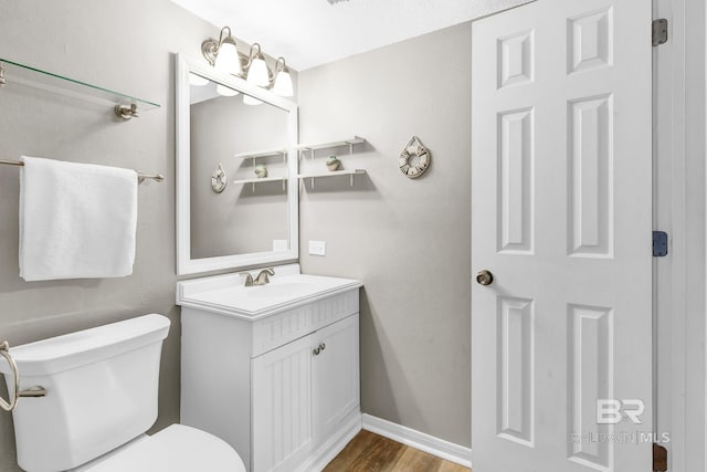 half bathroom featuring wood finished floors, vanity, toilet, and baseboards