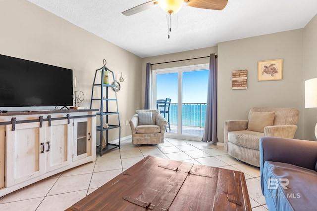 living room featuring a ceiling fan, a textured ceiling, baseboards, and light tile patterned floors