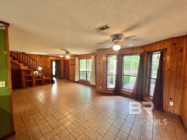 unfurnished living room featuring a ceiling fan, wood walls, visible vents, and light tile patterned floors