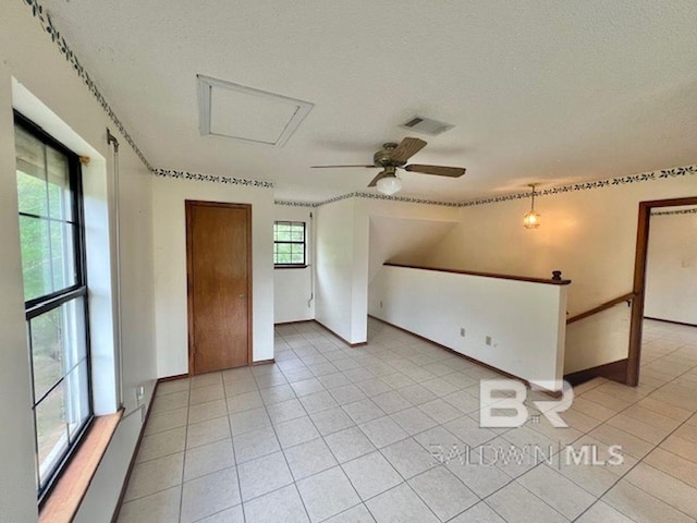 empty room with a textured ceiling, a ceiling fan, baseboards, light tile patterned floors, and visible vents