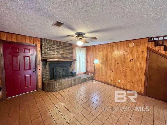 unfurnished living room featuring tile patterned flooring, a fireplace, wood walls, a ceiling fan, and visible vents
