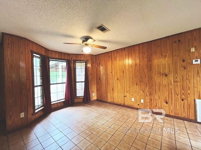 unfurnished room featuring visible vents, wood walls, baseboards, and ceiling fan