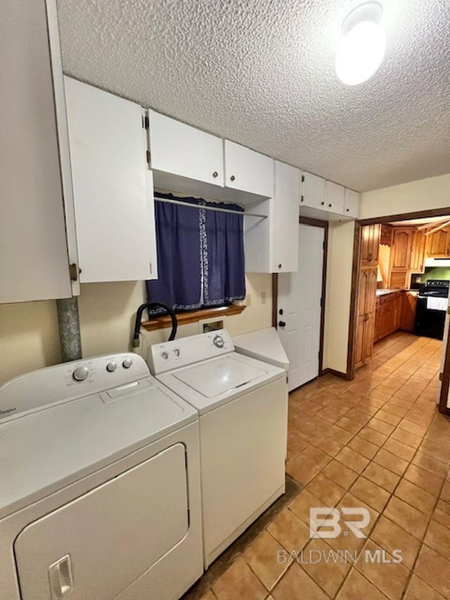 washroom with a textured ceiling, cabinet space, light tile patterned flooring, and independent washer and dryer