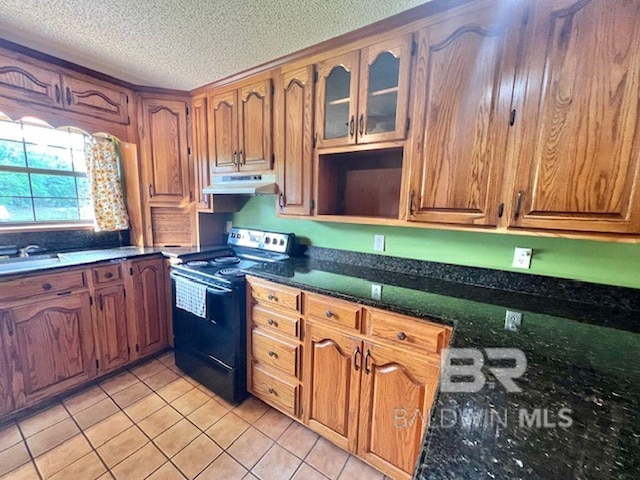kitchen with brown cabinetry, black electric range oven, light tile patterned flooring, a textured ceiling, and under cabinet range hood