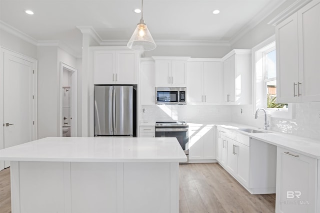 kitchen featuring a kitchen island, appliances with stainless steel finishes, crown molding, light wood-style floors, and a sink