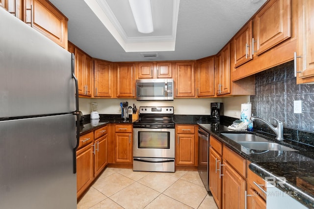 kitchen with a tray ceiling, stainless steel appliances, brown cabinetry, ornamental molding, and a sink