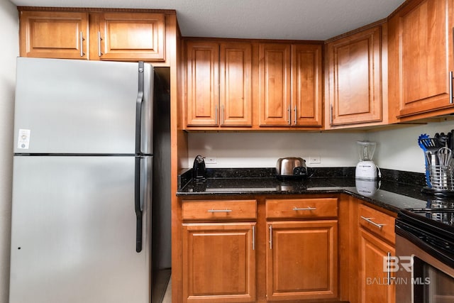 kitchen with brown cabinets, dark stone countertops, and freestanding refrigerator