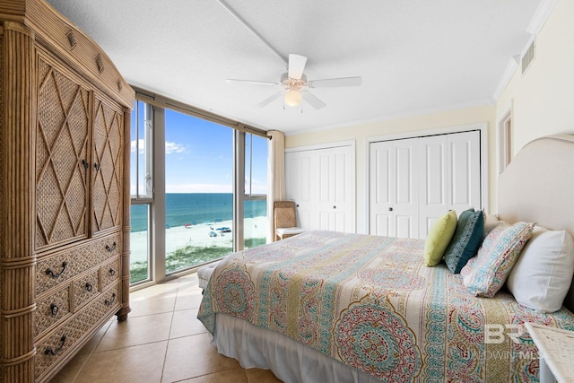 bedroom with light tile patterned floors, a water view, visible vents, multiple closets, and expansive windows