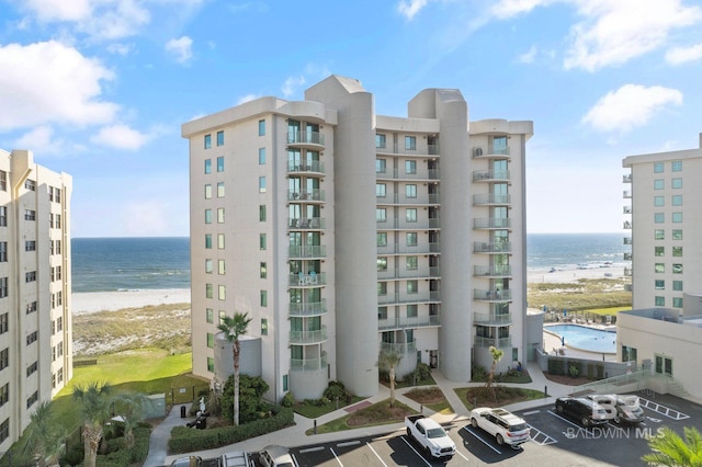 view of building exterior with uncovered parking, a water view, and a beach view