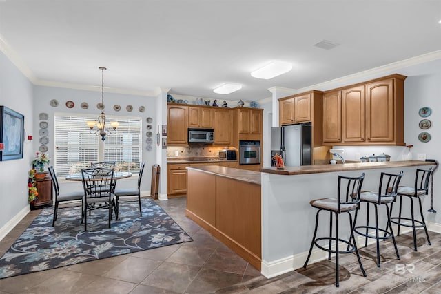 kitchen featuring appliances with stainless steel finishes, a kitchen breakfast bar, crown molding, a notable chandelier, and hanging light fixtures