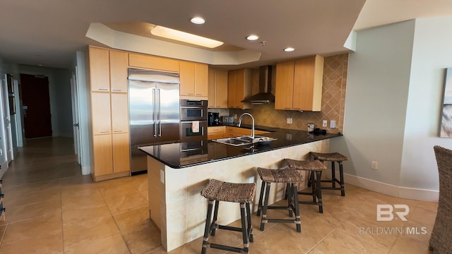 kitchen with dark countertops, a peninsula, stainless steel appliances, wall chimney range hood, and a sink