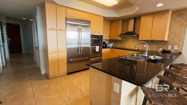 kitchen with a peninsula, wall chimney exhaust hood, stainless steel appliances, and a sink