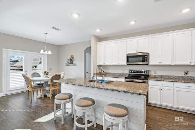 kitchen with decorative light fixtures, white cabinetry, dark stone countertops, a center island with sink, and appliances with stainless steel finishes