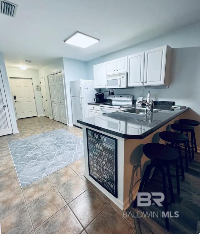 kitchen with white appliances, kitchen peninsula, light tile patterned floors, white cabinets, and sink